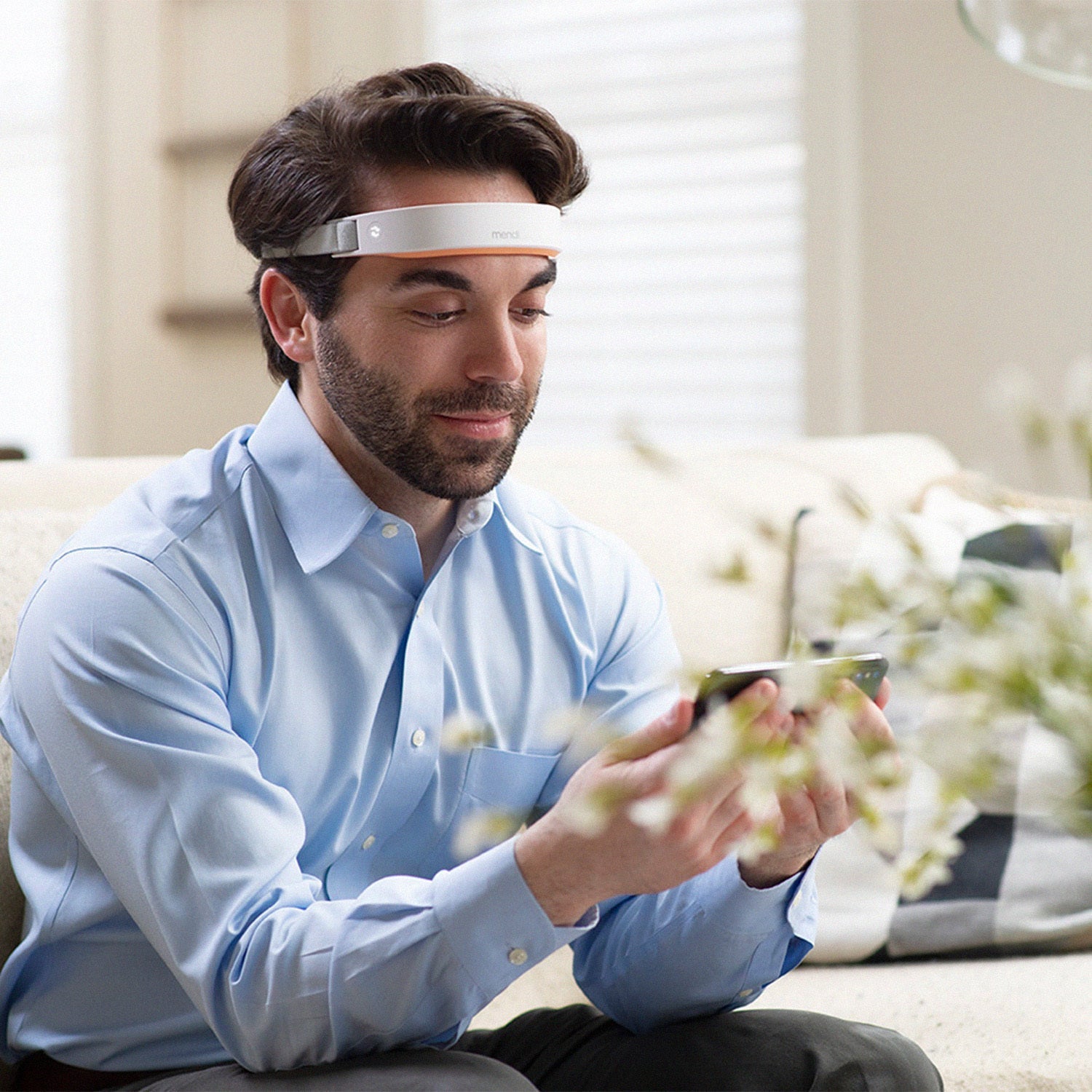 Bearded man wearing The Mendi Headset on his forehead while following a session on his phone