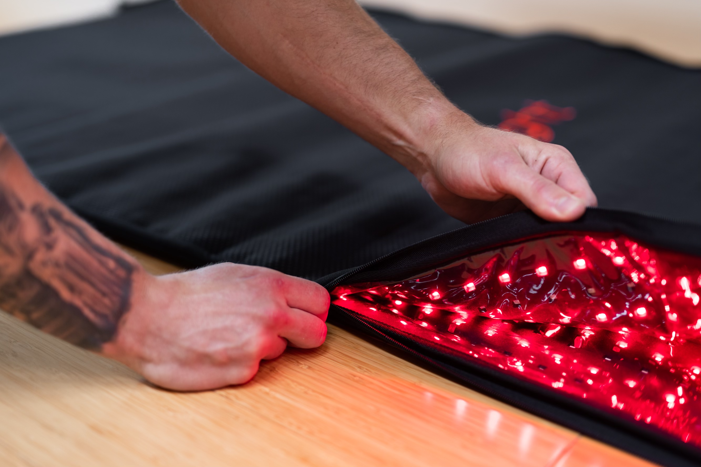 Hands peel back the BioLight Cocoon pod's black cover to reveal its red LED array up close