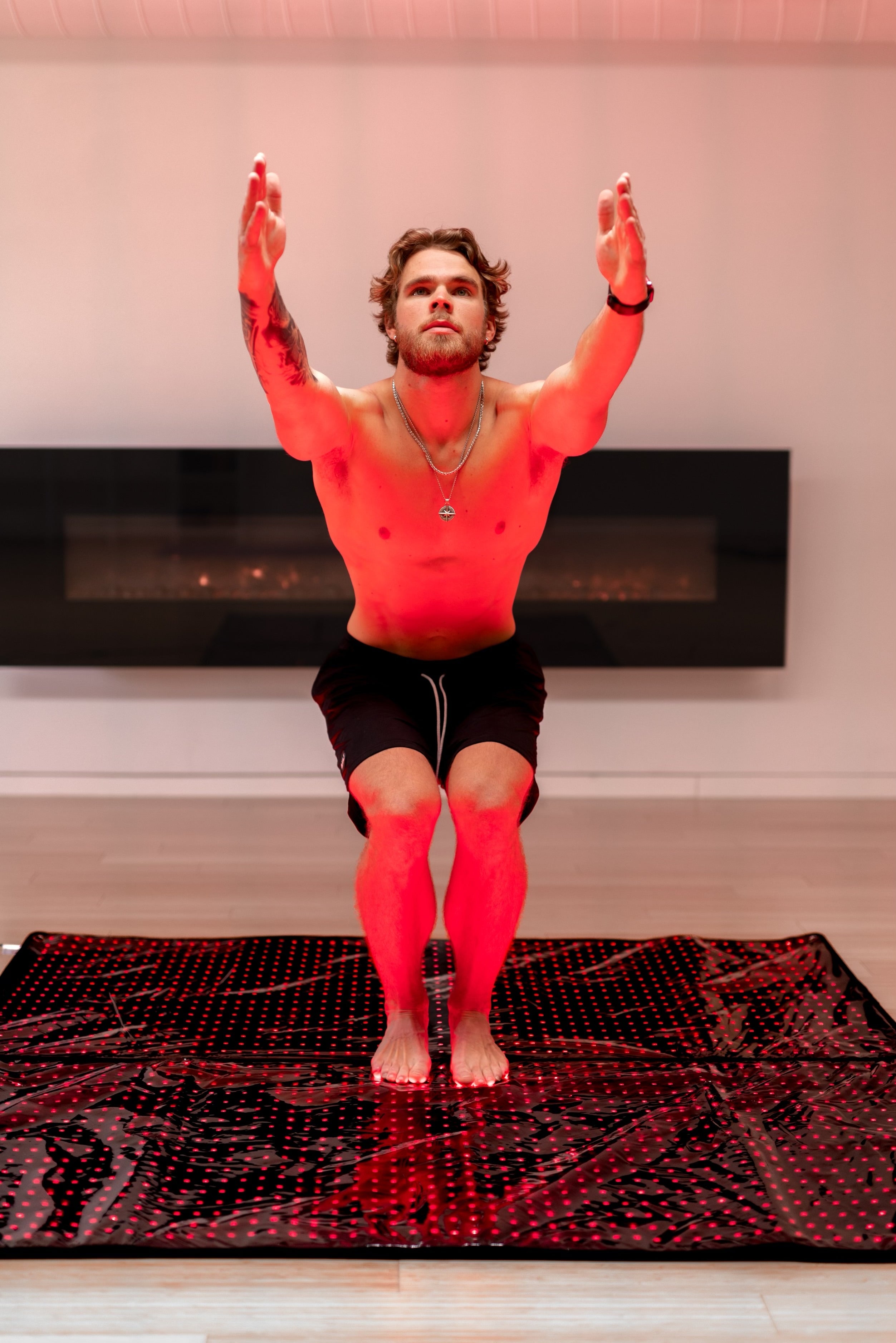 Man squats with arms raised on the open BioLight Cocoon pod, feet on its red-lit LED surface