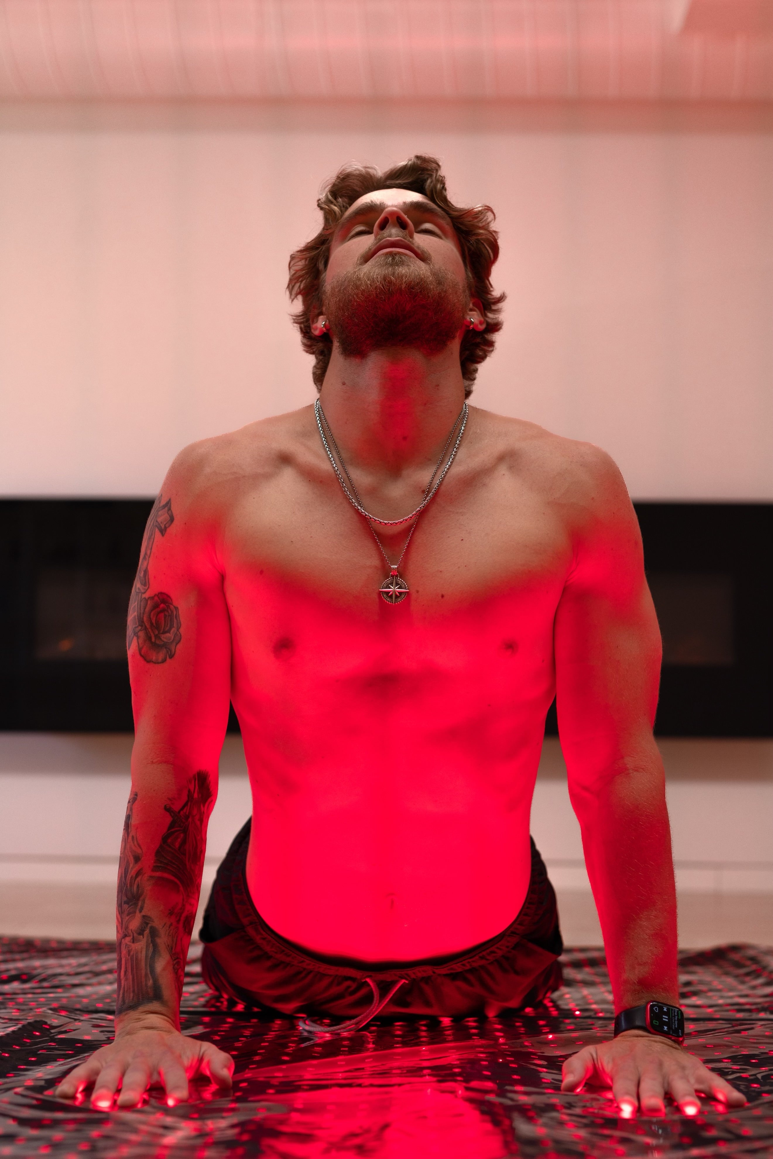 Front view of a man in upward dog pose on the BioLight Cocoon pod, bathed in its red light