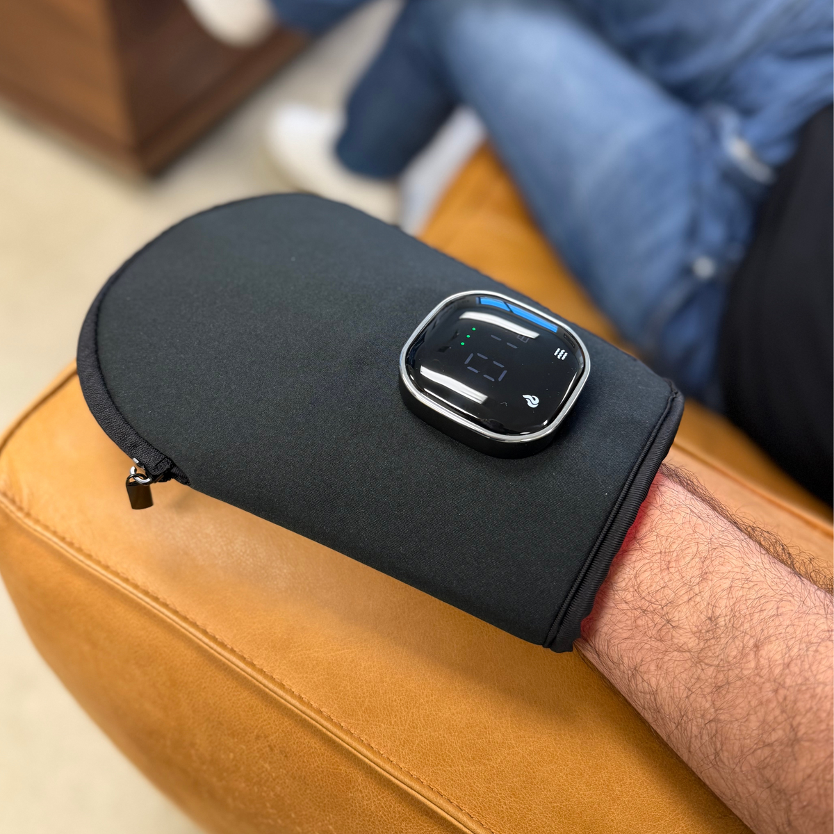 Hand resting inside the TheraGlove on a sofa arm, controller on top
