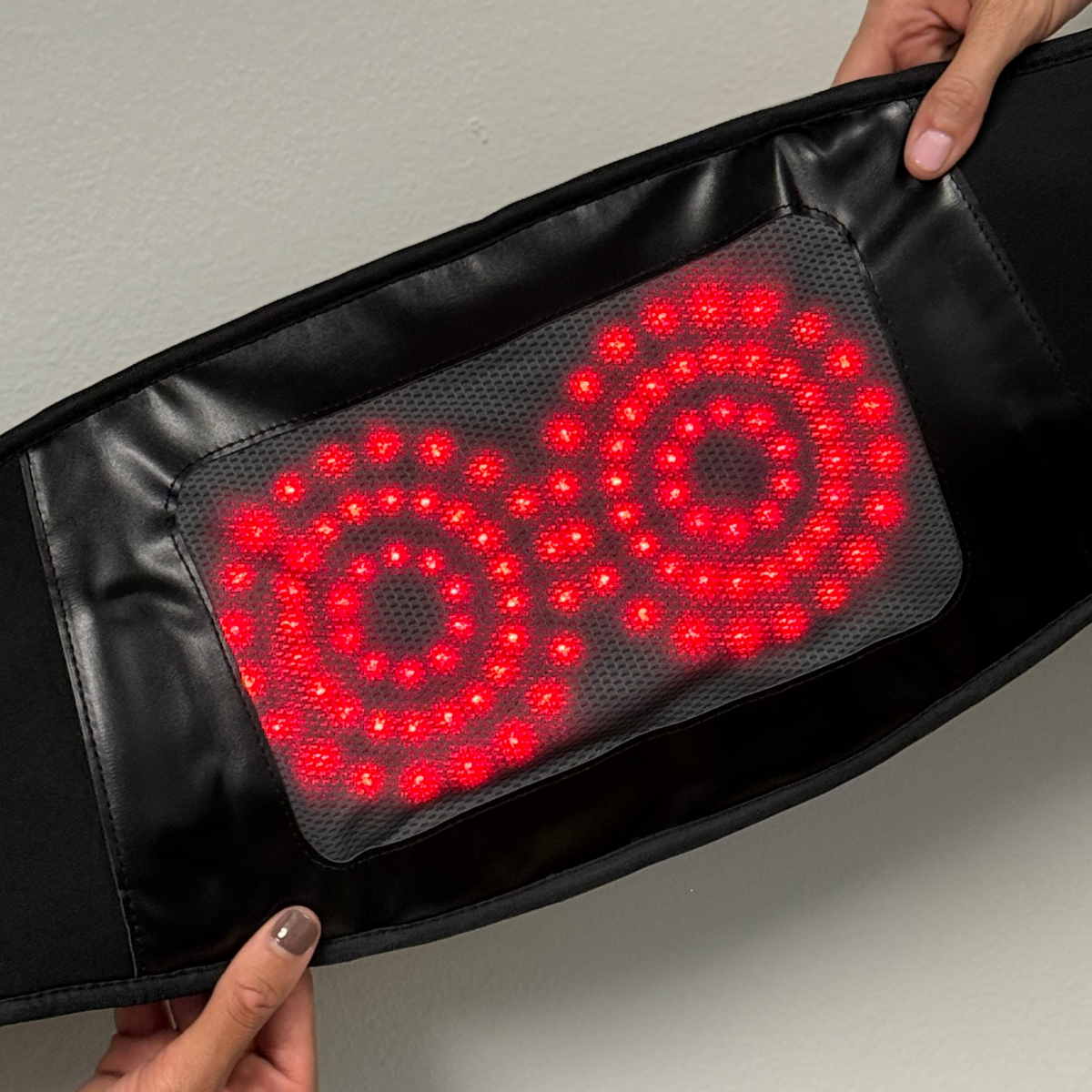 Hands holding the TheraBelt open to show two circular arrays of red LEDs