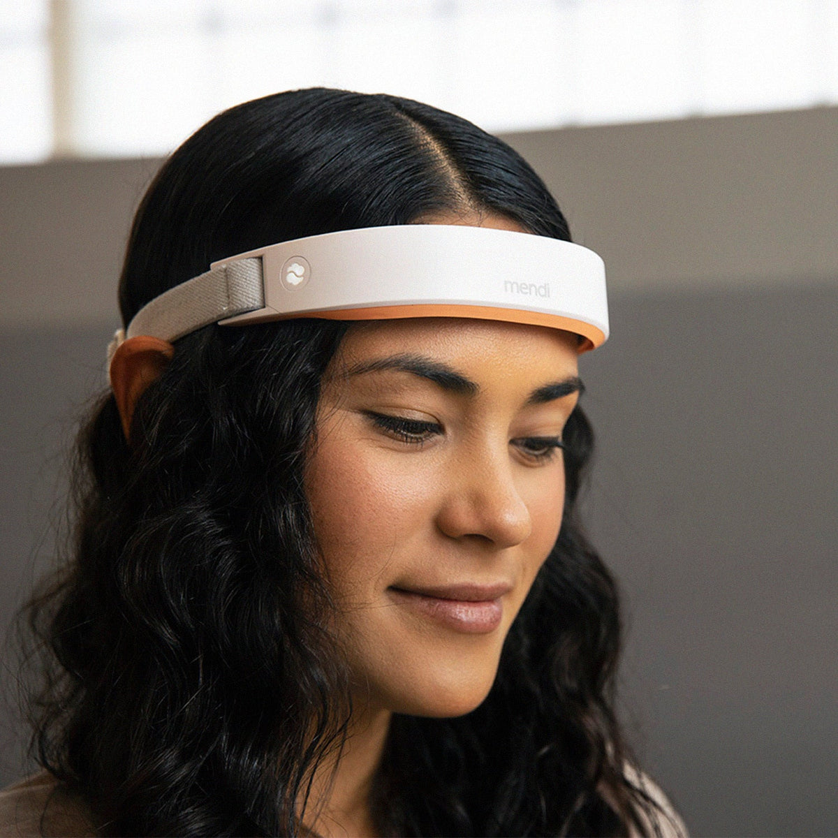 Woman with dark wavy hair wearing The Mendi Headset across her forehead, eyes lowered