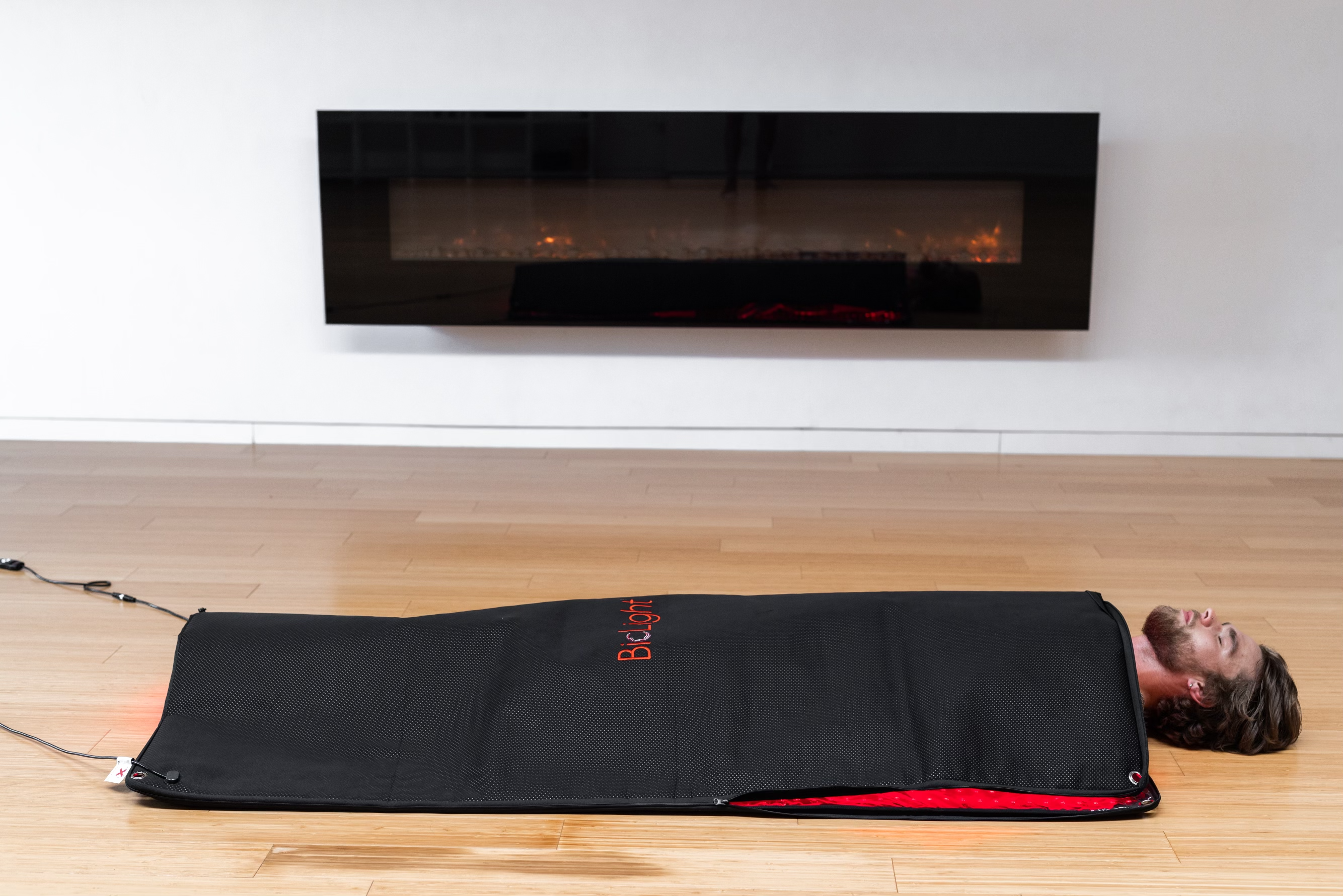 BioLight Cocoon red light therapy pod closed on a wood floor with a man lying inside, head resting outside