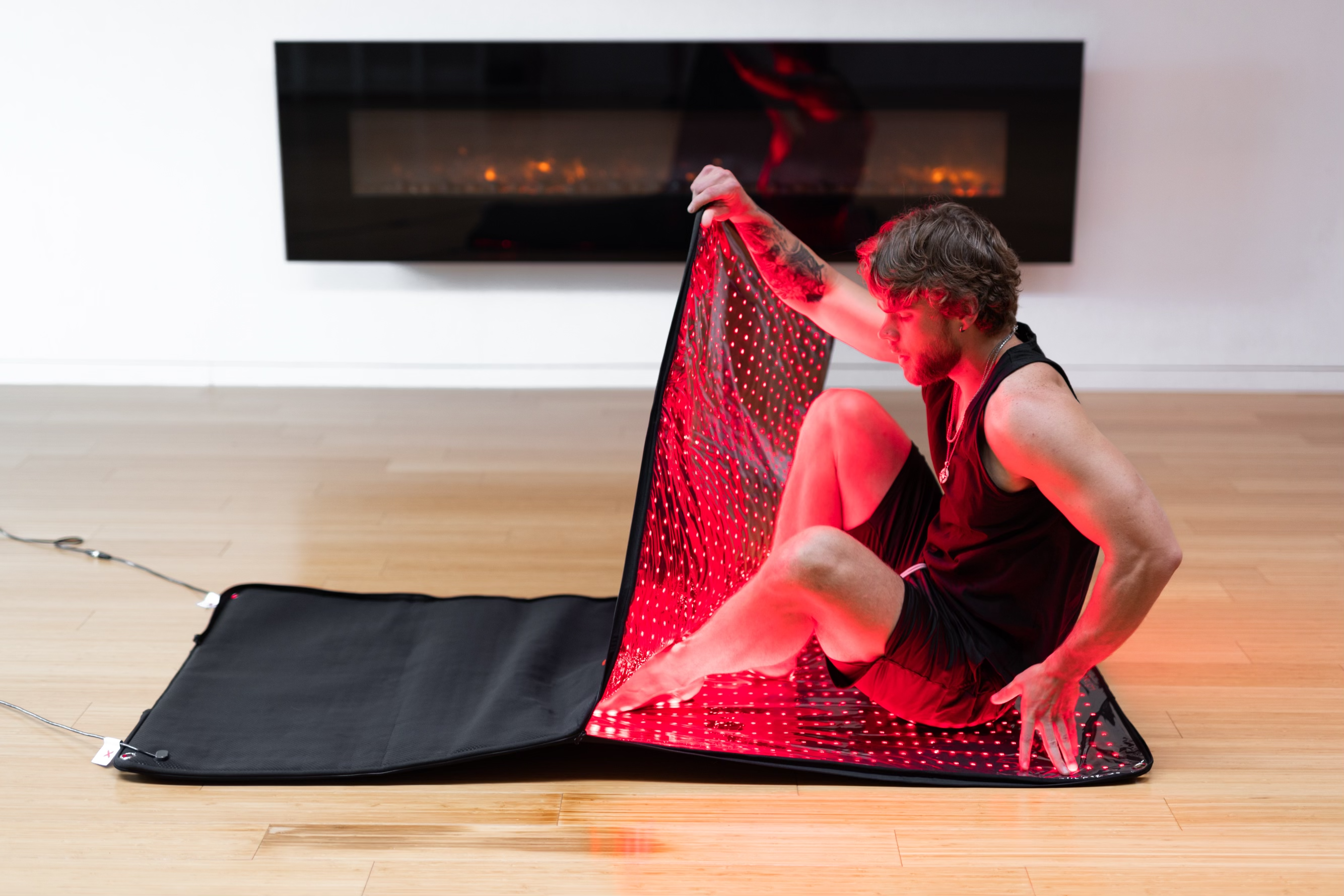 Seated man raises the BioLight Cocoon pod's flexible LED panel, showing rows of red lights inside