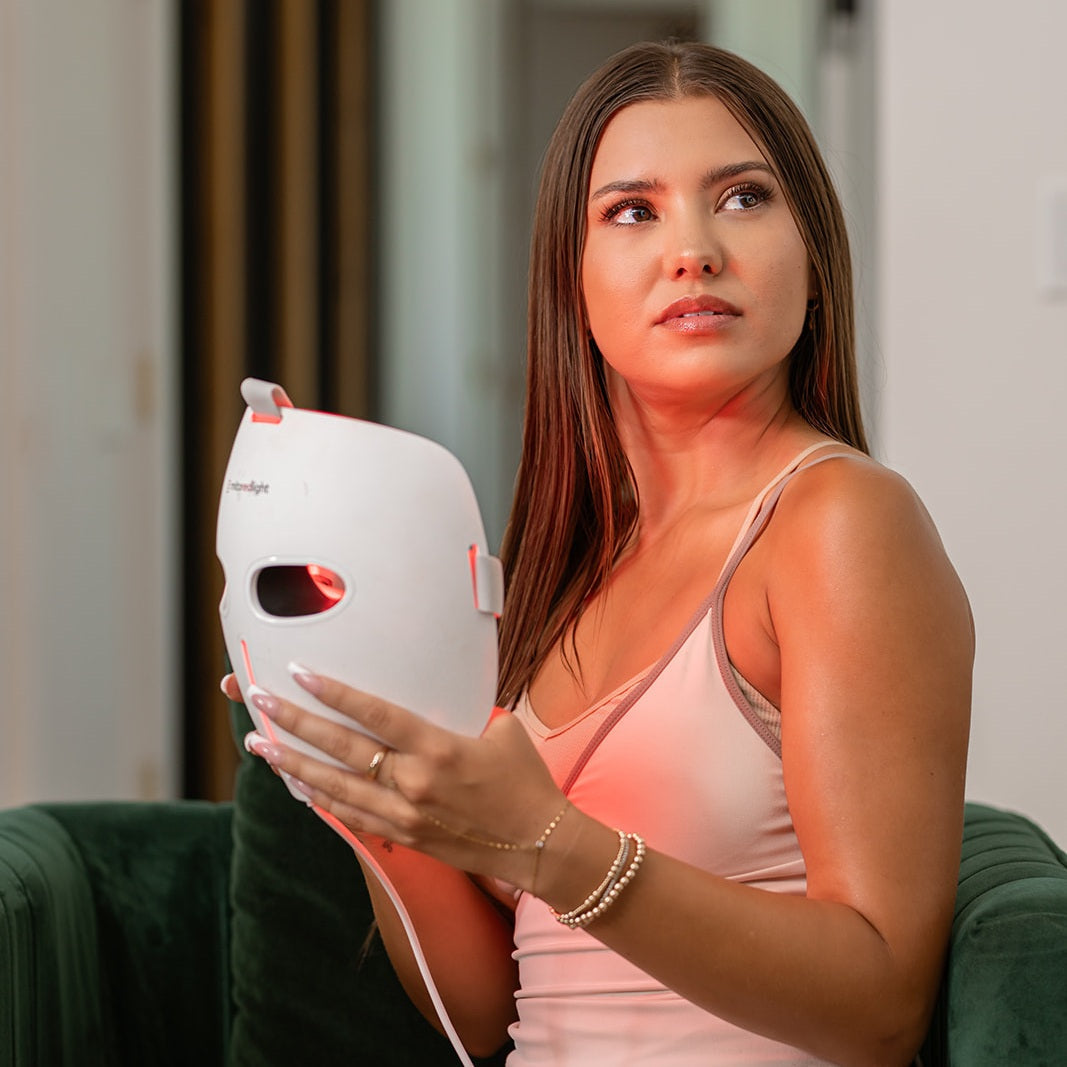 MitoGLOW red light therapy mask held glowing in a woman's hands