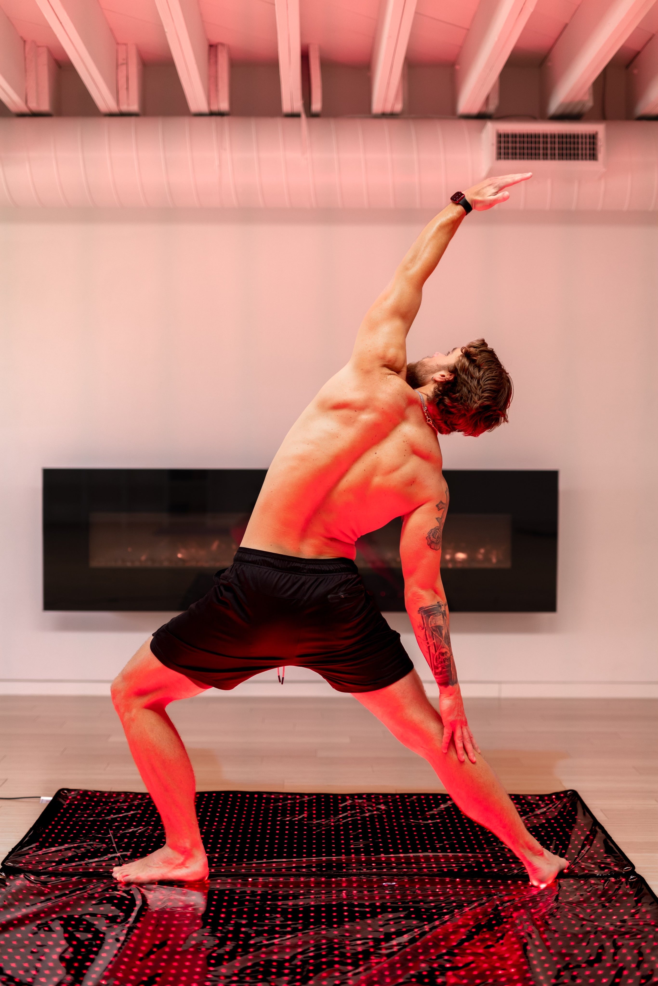 Man stretches in a standing side bend on the BioLight Cocoon pod's red-lit LED mat