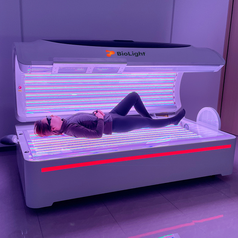 BioLight Helios System light therapy bed open with a woman lying on the multicolor LED base